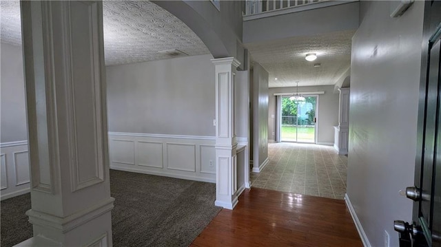corridor with decorative columns, arched walkways, a textured ceiling, wood finished floors, and baseboards