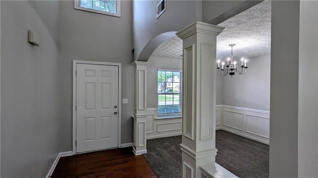 entryway with ornate columns, arched walkways, a wainscoted wall, a chandelier, and a textured ceiling