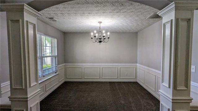 spare room featuring a chandelier, a wainscoted wall, dark carpet, a decorative wall, and ornate columns