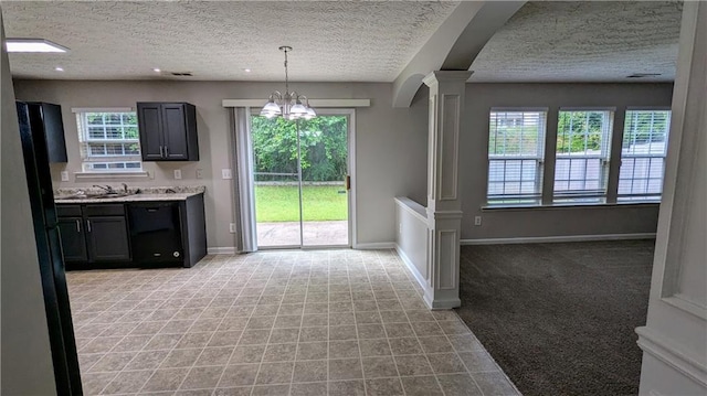unfurnished dining area with decorative columns, a chandelier, a textured ceiling, baseboards, and light colored carpet