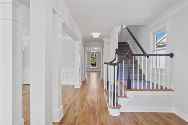 corridor with ornate columns, crown molding, and light hardwood / wood-style floors