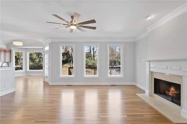 unfurnished living room with a fireplace, sink, ceiling fan, light hardwood / wood-style floors, and crown molding