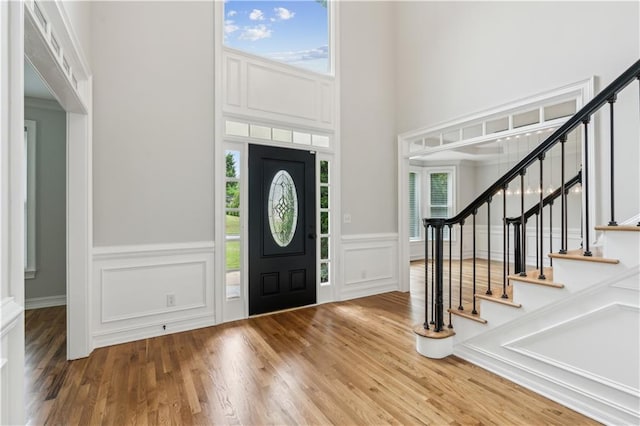 foyer entrance featuring a towering ceiling, wood finished floors, stairway, a wainscoted wall, and a decorative wall