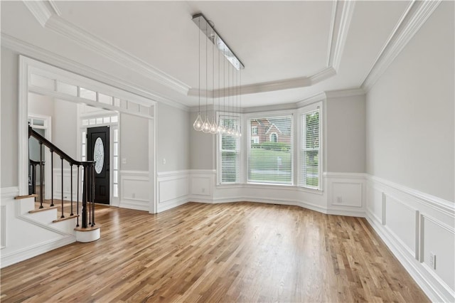 entrance foyer featuring light wood finished floors, a decorative wall, a tray ceiling, and stairway