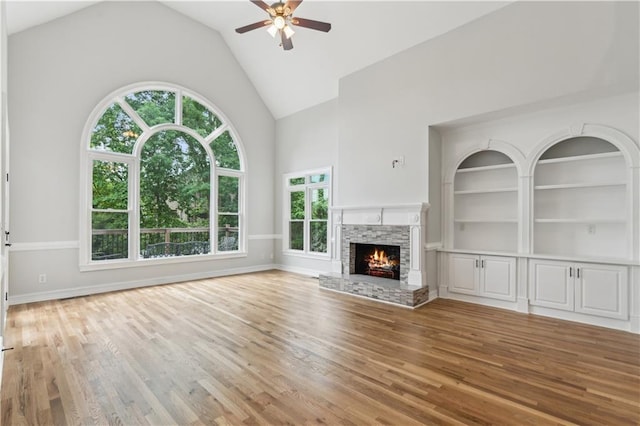 unfurnished living room featuring light wood-type flooring, a ceiling fan, a fireplace, and high vaulted ceiling