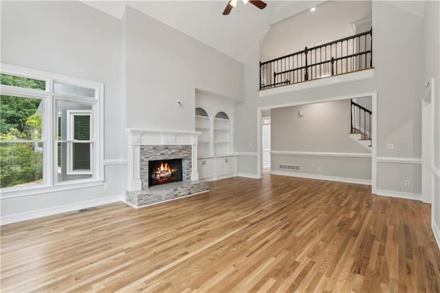 unfurnished living room featuring a fireplace, high vaulted ceiling, stairway, built in shelves, and a ceiling fan