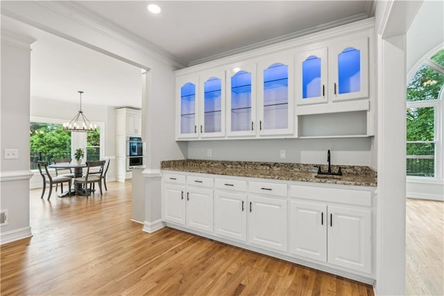 bar with ornamental molding, double oven, light wood-style flooring, and a wealth of natural light