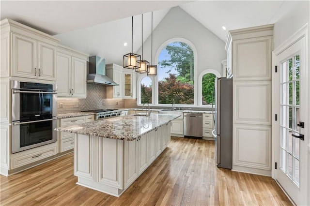 kitchen featuring wall chimney range hood, stainless steel appliances, a sink, and a healthy amount of sunlight