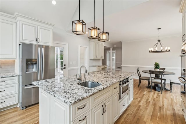 kitchen featuring white cabinets, a sink, light wood-style flooring, stainless steel appliances, and pendant lighting