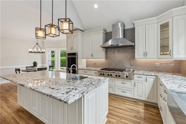 kitchen with appliances with stainless steel finishes, light stone counters, a sink, wall chimney exhaust hood, and lofted ceiling