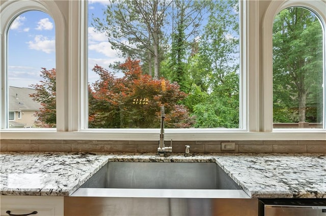 details with a sink, light stone counters, and stainless steel dishwasher