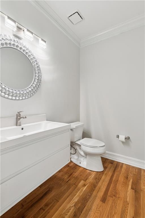 half bath featuring crown molding, vanity, toilet, wood finished floors, and visible vents