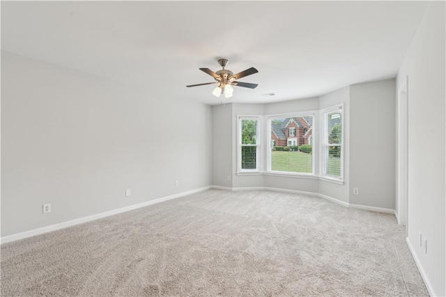 empty room featuring light colored carpet, baseboards, and ceiling fan