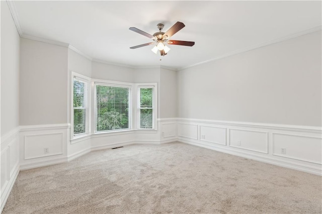carpeted spare room featuring crown molding, a decorative wall, ceiling fan, and wainscoting