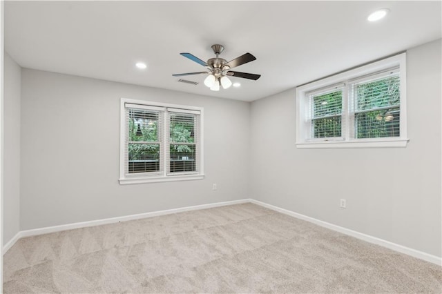 carpeted spare room featuring visible vents, a ceiling fan, baseboards, and plenty of natural light