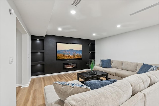 living area featuring visible vents, a glass covered fireplace, wood finished floors, recessed lighting, and built in shelves