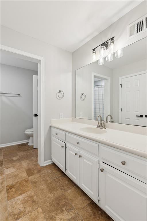 bathroom with stone finish floor, visible vents, vanity, baseboards, and toilet