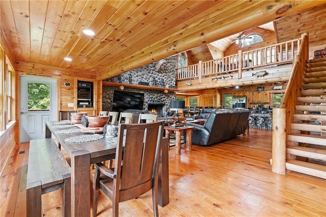 dining room with a stone fireplace, light wood-type flooring, wood ceiling, and vaulted ceiling