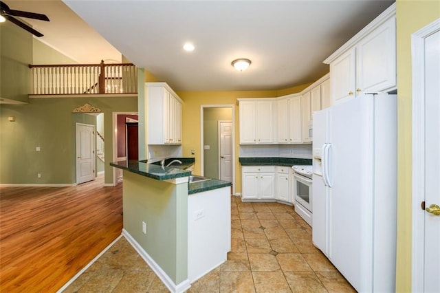 kitchen with white appliances, a peninsula, dark countertops, white cabinets, and ceiling fan