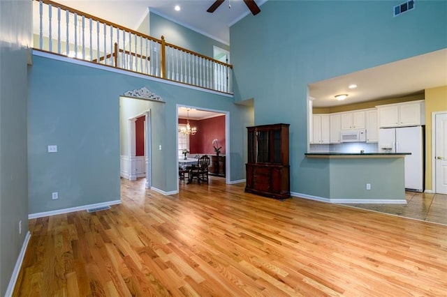 unfurnished living room with a high ceiling, ceiling fan, light wood-type flooring, baseboards, and a chandelier