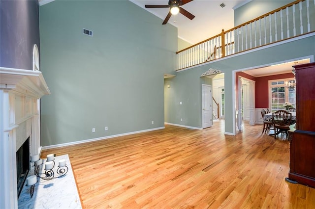 unfurnished living room featuring a ceiling fan, high vaulted ceiling, light wood-style flooring, a fireplace, and baseboards