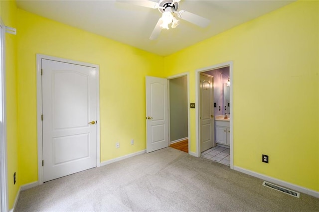 unfurnished bedroom with light carpet, ensuite bath, baseboards, and ceiling fan