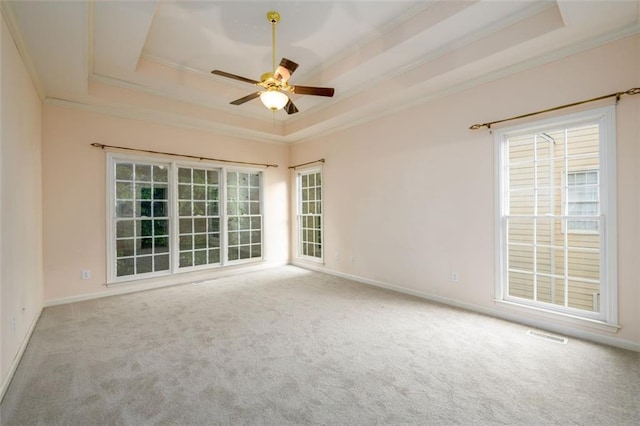 carpeted spare room featuring a tray ceiling, crown molding, ceiling fan, and baseboards