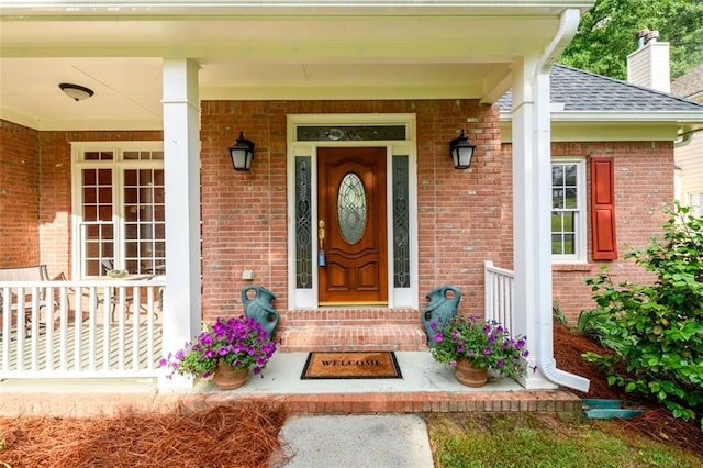 view of exterior entry featuring brick siding, roof with shingles, and a chimney