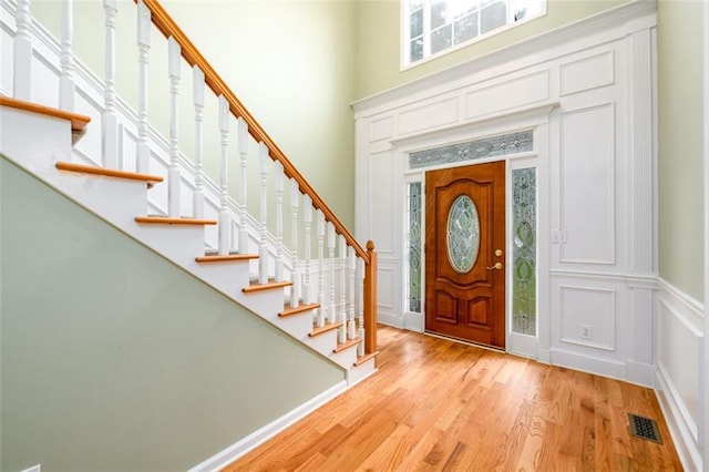 entrance foyer with a high ceiling, a decorative wall, stairway, and light wood-type flooring