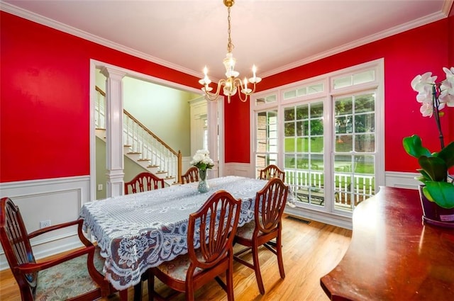 dining area featuring a wainscoted wall, a chandelier, wood finished floors, crown molding, and a decorative wall