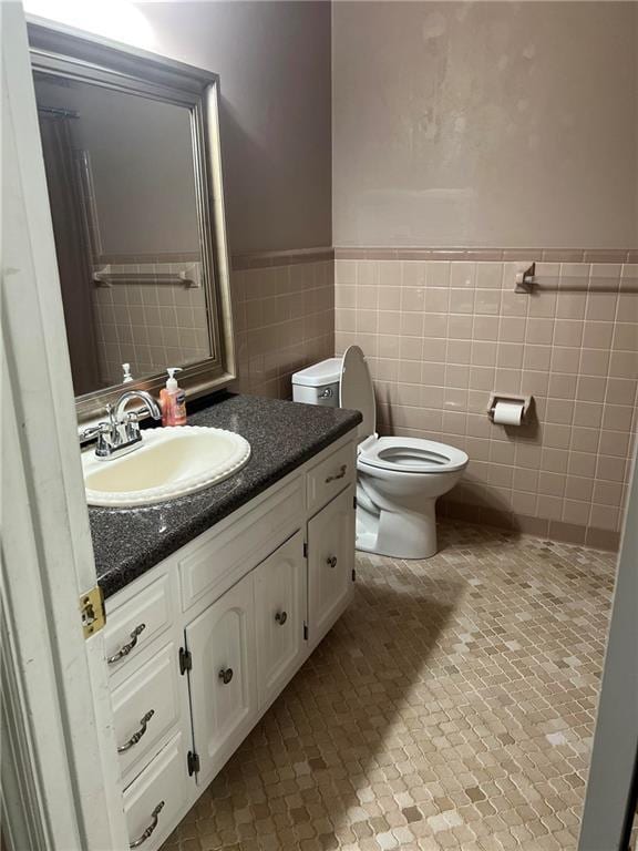 bathroom featuring vanity, tile walls, and toilet