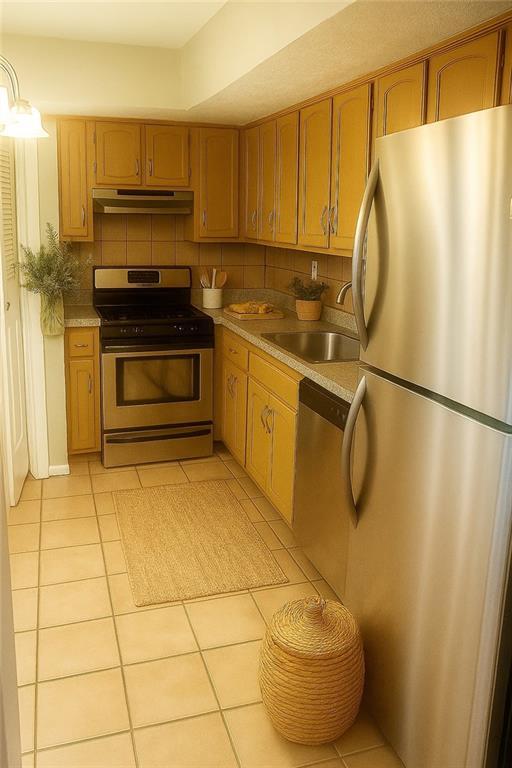 5581 Marbut Rd, Lithonia, GA 30058 - kitchen with appliances with stainless steel finishes, under cabinet range hood, light tile patterned flooring, backsplash, and light countertops