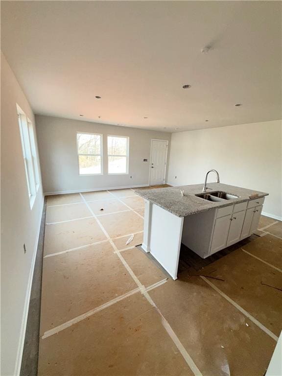 kitchen with open floor plan, a center island with sink, white cabinetry, and a sink