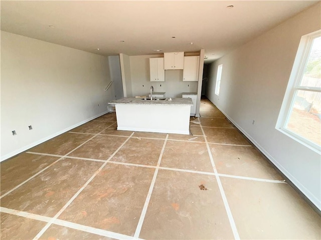 kitchen with white cabinetry, light countertops, a center island with sink, and a sink