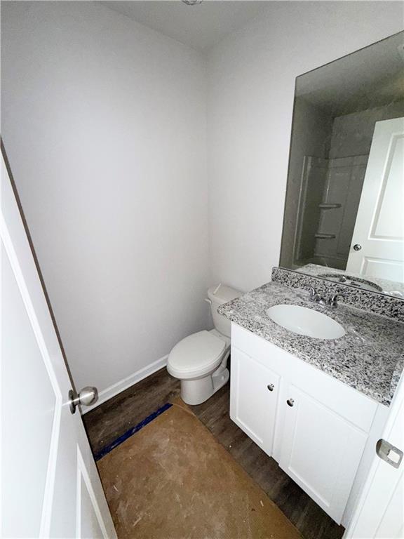 bathroom with baseboards, walk in shower, toilet, wood finished floors, and vanity