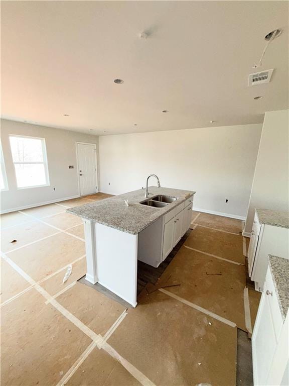 kitchen featuring visible vents, a sink, light stone counters, white cabinetry, and a kitchen island with sink