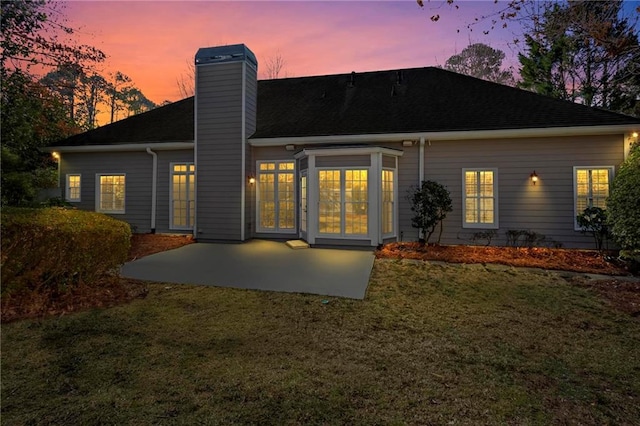 back of property at dusk featuring a patio area, a lawn, and a chimney