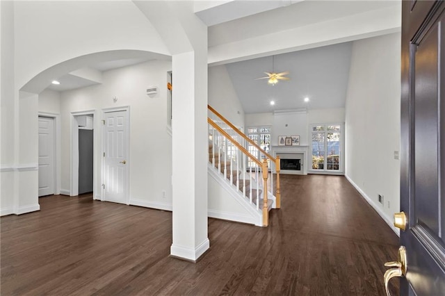 foyer with arched walkways, dark wood-style floors, a fireplace, and baseboards