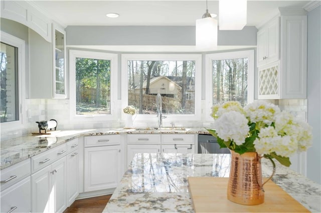 kitchen featuring tasteful backsplash, white cabinets, light stone counters, glass insert cabinets, and a sink