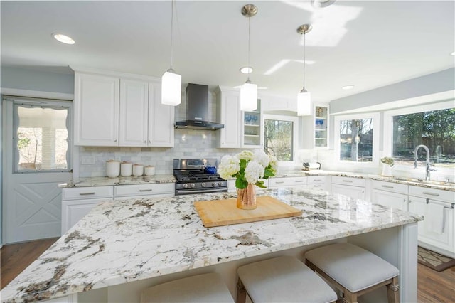 kitchen featuring stainless steel gas stove, wall chimney exhaust hood, a sink, and white cabinets