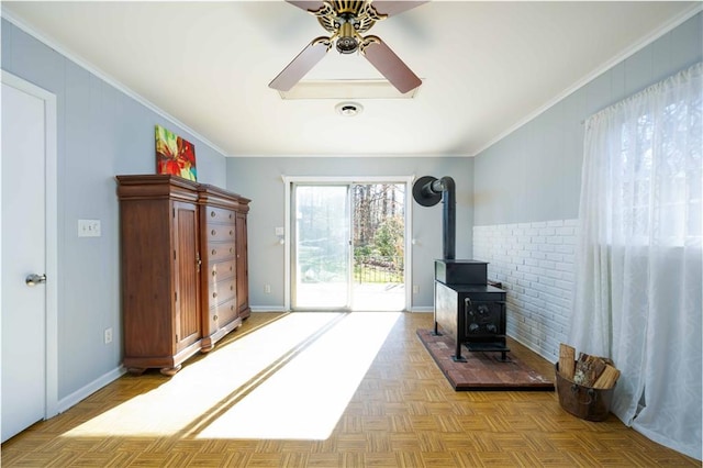 interior space featuring ornamental molding, a wood stove, baseboards, and a ceiling fan