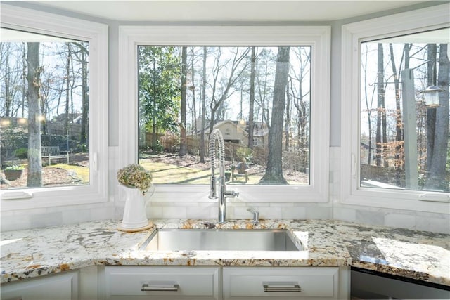 interior space with white cabinetry, a sink, dishwasher, and light stone countertops