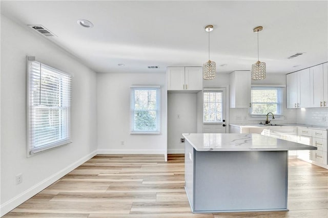 2502 Tupelo St SE, Atlanta, GA 30317 - kitchen with a sink, white cabinetry, a center island, light wood-style floors, and hanging light fixtures