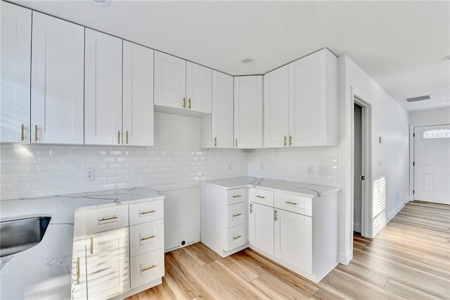 2502 Tupelo St SE, Atlanta, GA 30317 - kitchen featuring light stone countertops, light wood-style floors, white cabinetry, and decorative backsplash