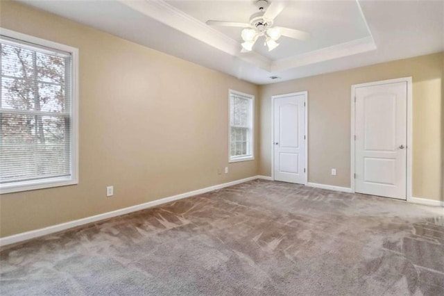 unfurnished bedroom with light carpet, a tray ceiling, multiple windows, and ceiling fan