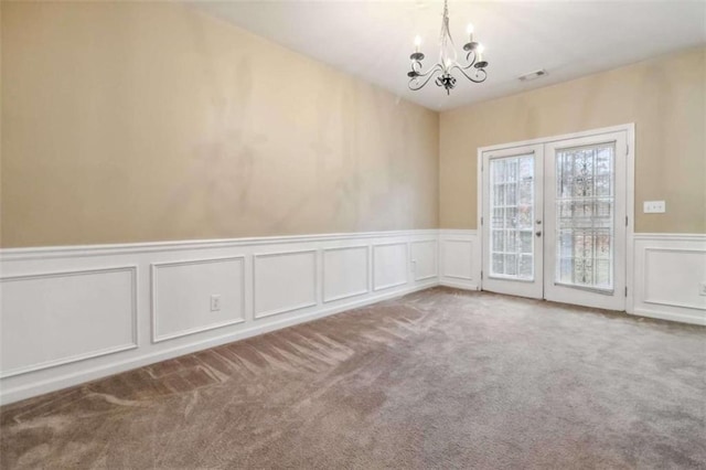 carpeted spare room with french doors and an inviting chandelier