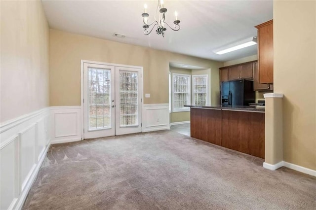 kitchen with an inviting chandelier, black fridge, kitchen peninsula, light colored carpet, and decorative light fixtures