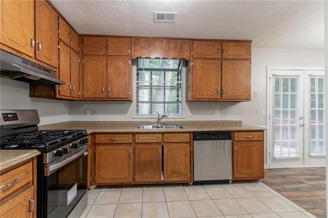 5218 Tina Ct, Stone Mountain, GA 30083 - kitchen featuring stainless steel appliances, a sink, under cabinet range hood, brown cabinetry, and a textured ceiling