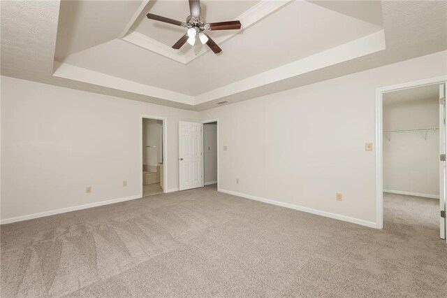 unfurnished bedroom featuring a spacious closet, light carpet, ceiling fan, and a raised ceiling