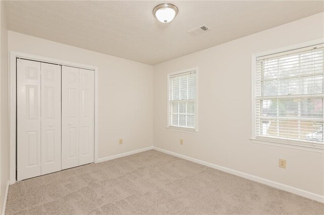 unfurnished bedroom featuring a closet, multiple windows, and light carpet
